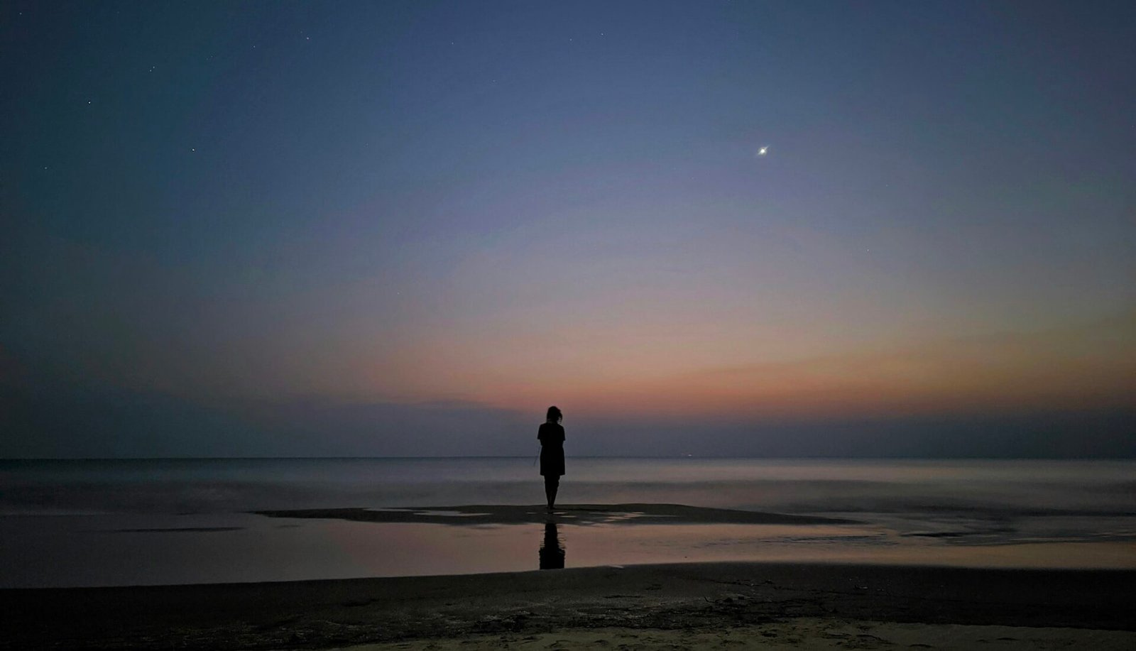A solitary person on the seashore beneath the evening sky.