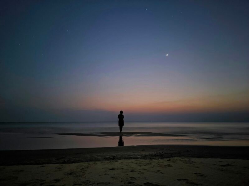 A solitary person on the seashore beneath the evening sky.
